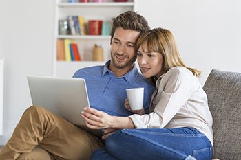 Happy man and woman on a couch looking at a laptop