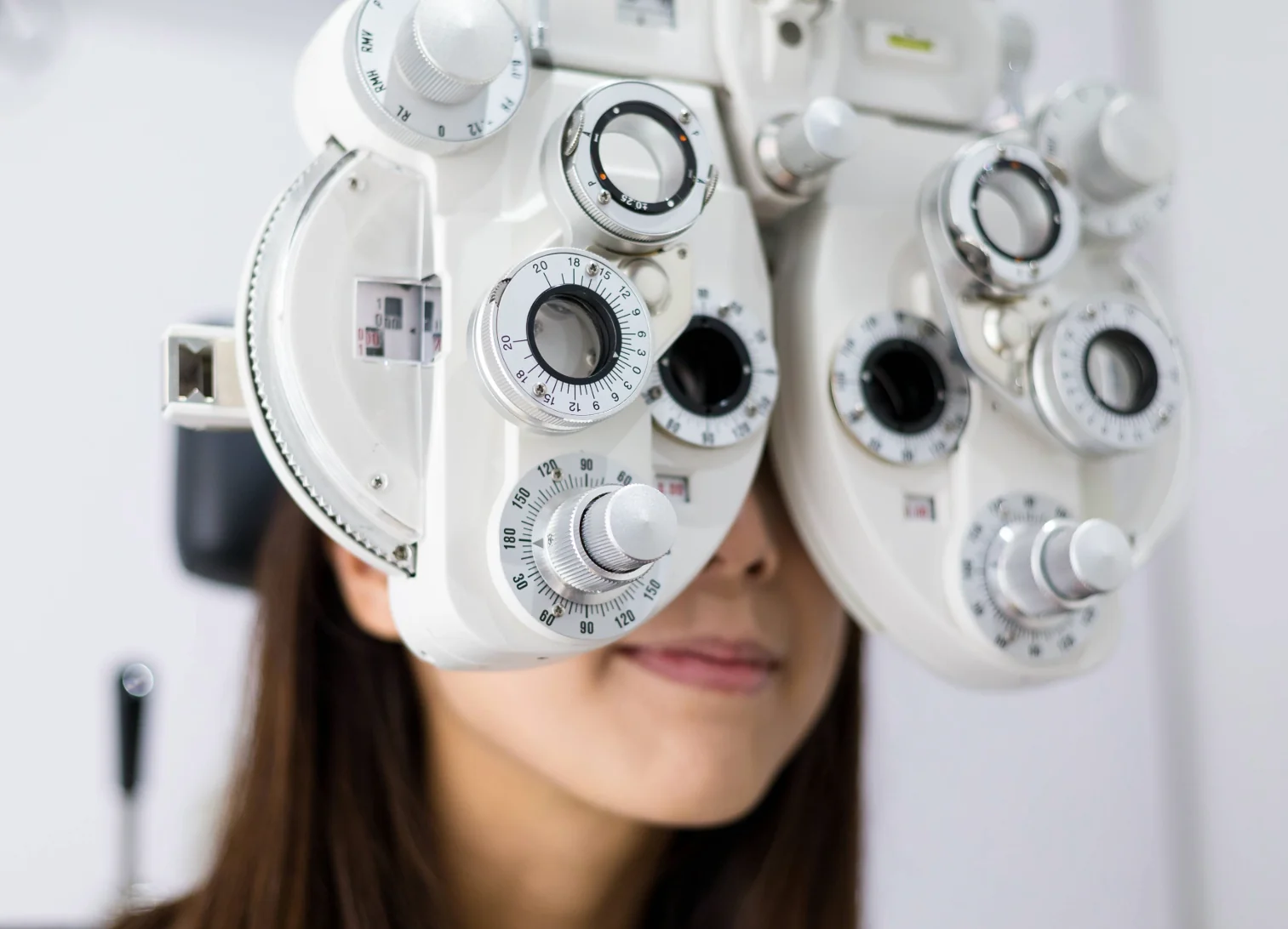 young woman looking through phoropter during eye exam